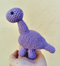 purple crochet dinosaur, sits in a persons hand