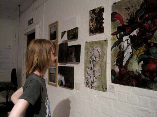 side angle of woman looking at painting of mushrooms on a wall with other various sized paintings 