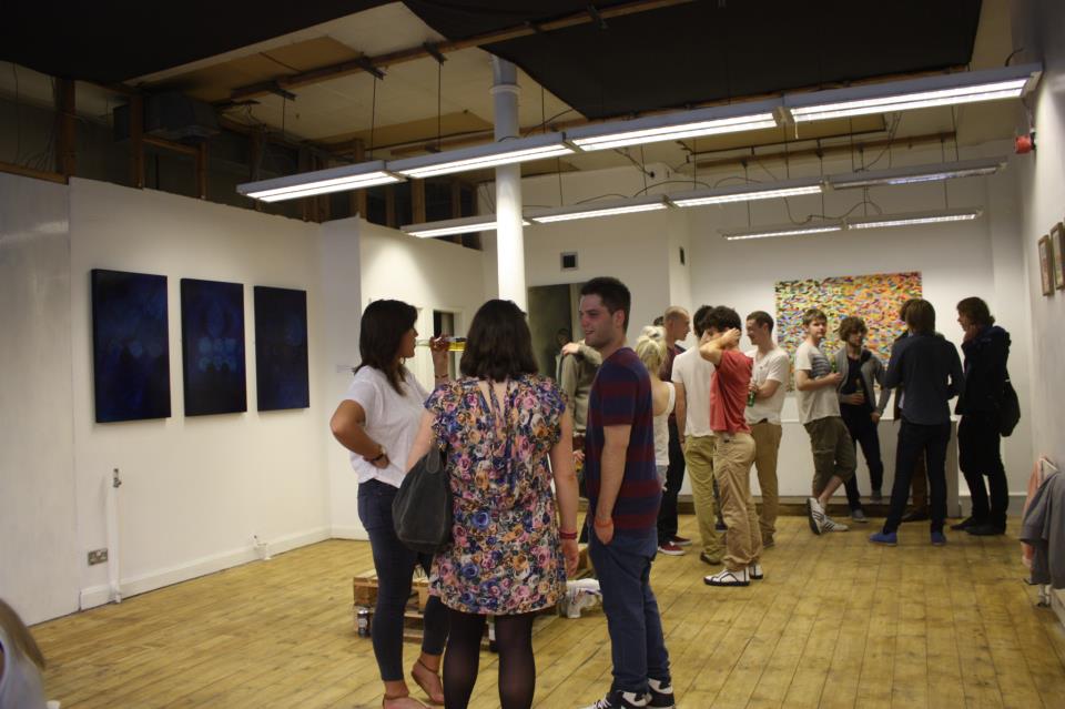 12 people stood in an art gallery, chatting in groups