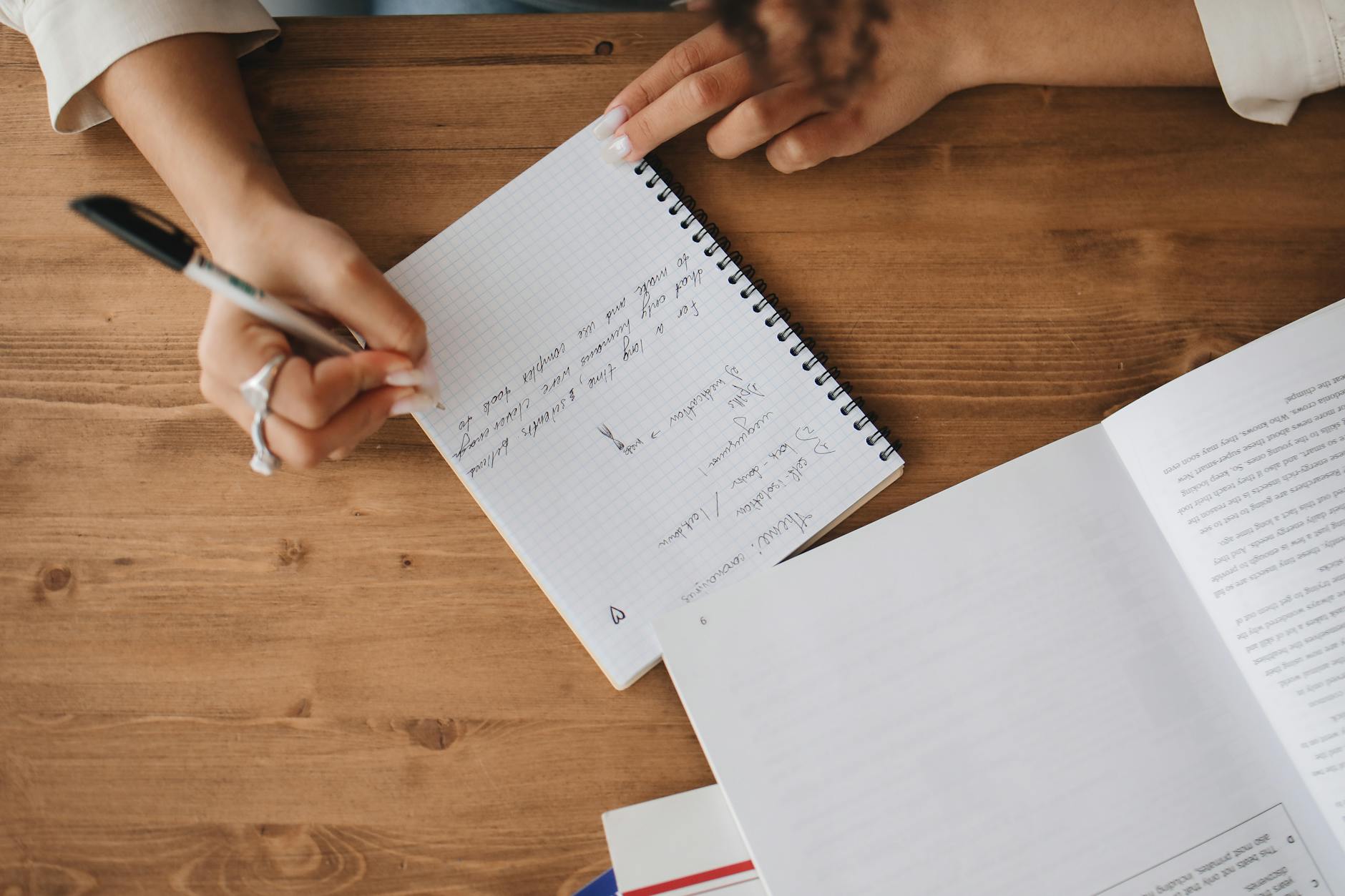 woman's hands writing in notepad at a wooden desk.