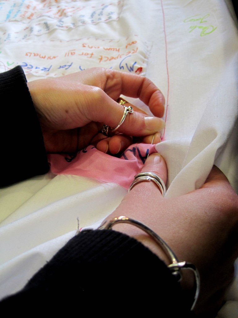 blue filter over pair of female hands using a sewing needle to stitch a piece of fabric