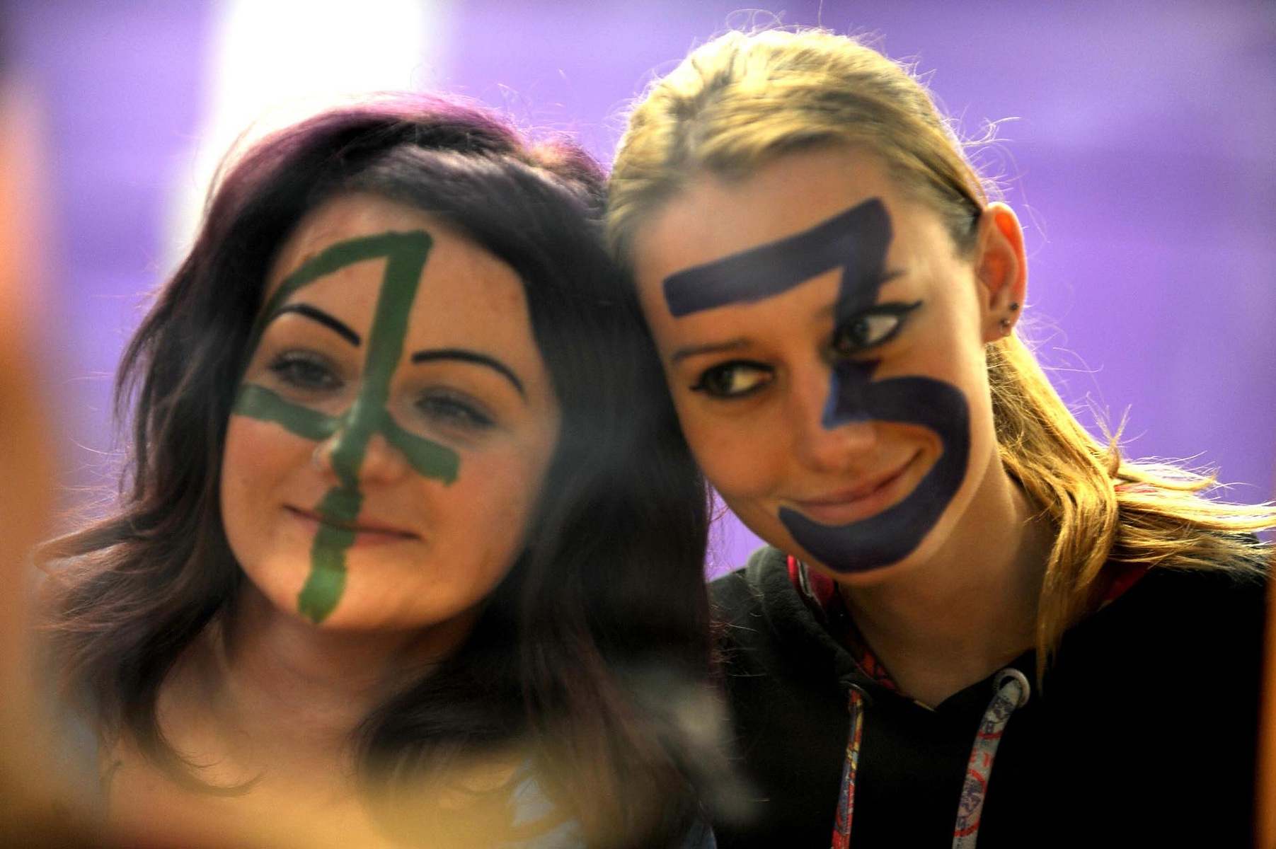 2 women in their 20s head shot, Emma has the number 4 face painted on her face, Amanda has the number 3 painted on her face