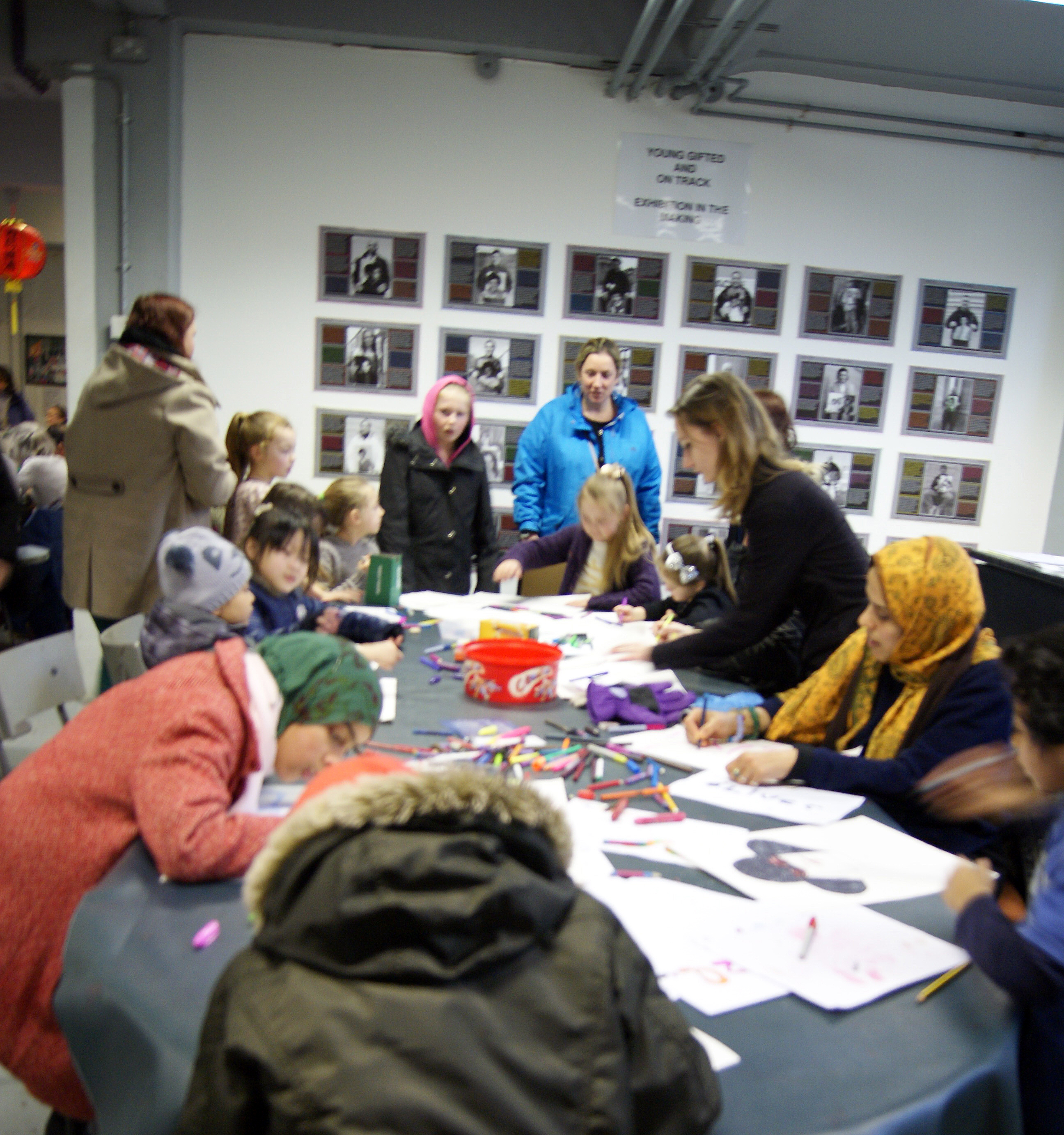 group of 12 kids sat around a table, drawing snakes, Amanda helping one kid