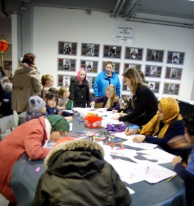 group of 12 kids sat around a table, drawing snakes, Amanda helping one kid