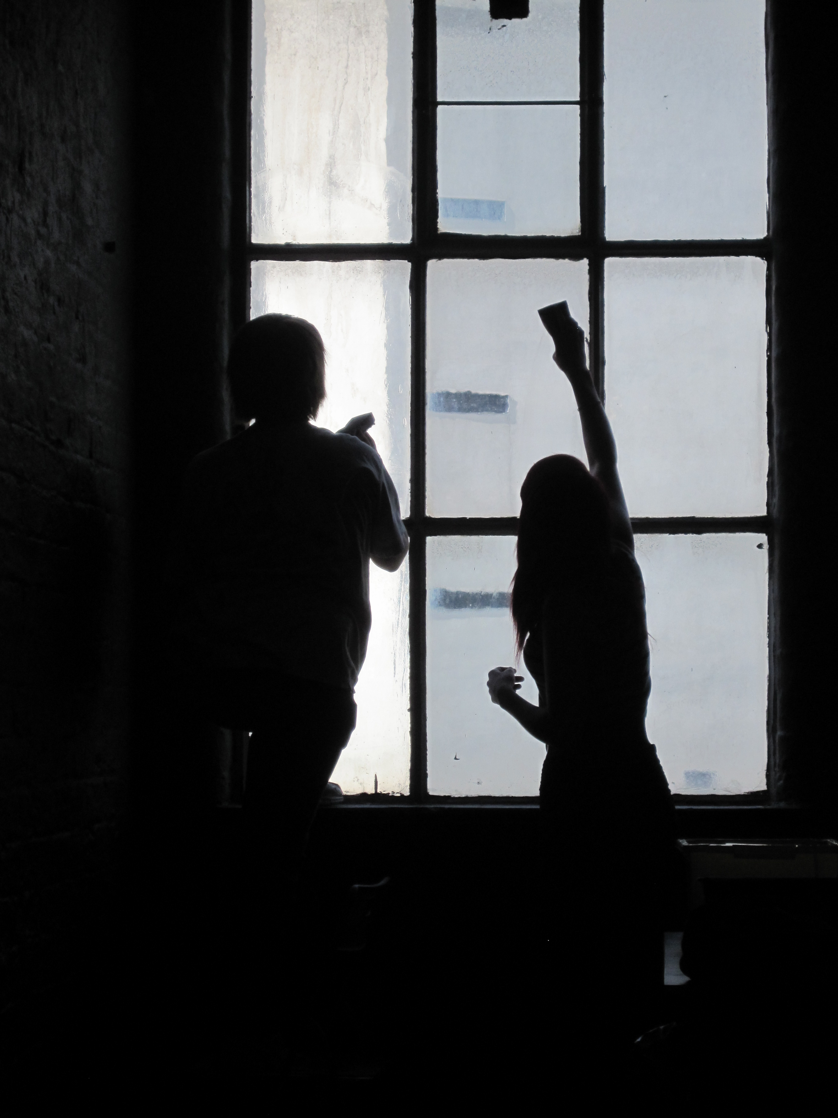 silhouette of 2 women wiping a large 8 panel window 