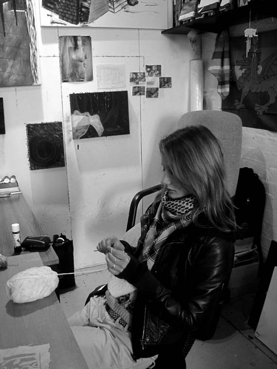 black and white photo of Amanda sat on a chair in a art studio space concentrating on crocheting 