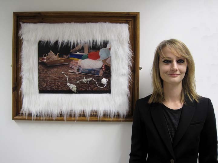 Amanda standing next to a white wall with a framed image of crochet and yarn.