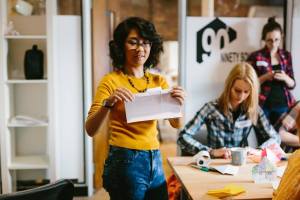 woman in foreground of art studio, folding paper in a demonstration. Women in the background concentrating on folding paper
